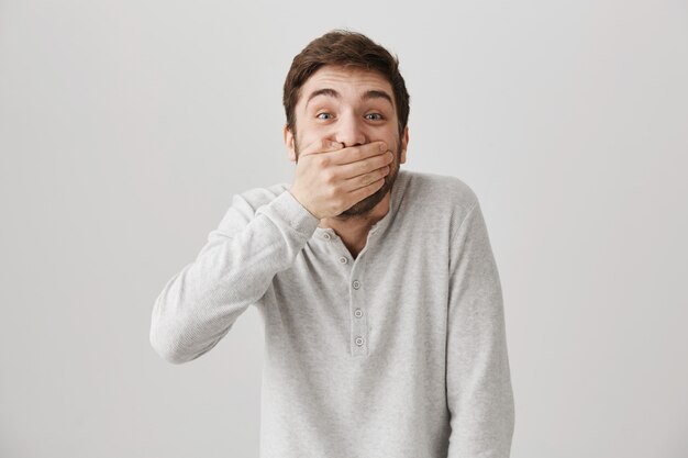 Speelse gelukkige knappe jongen lachen, mond dicht om niet te giechelen