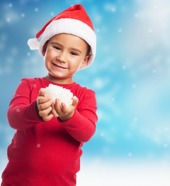 Speelse jongen met hoed van de Kerstman en sneeuw in handen