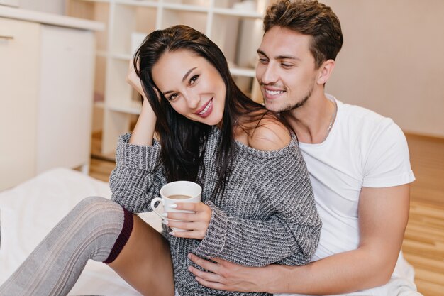 Speelse vrouw in grijze kleding ochtend doorbrengen met vriendje en genieten van warme koffie