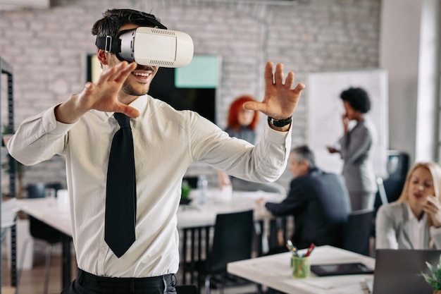 Speelse zakenman die een virtual reality-headset draagt en plezier heeft op kantoor Er zijn mensen op de achtergrond