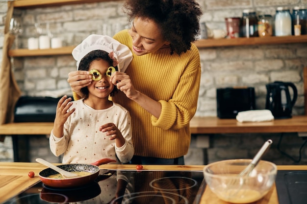 Speelse zwarte moeder en dochter die plezier hebben met eten tijdens het bereiden van een maaltijd in de keuken