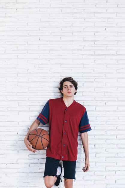 Speler met basketbal die op bakstenen muur leunt