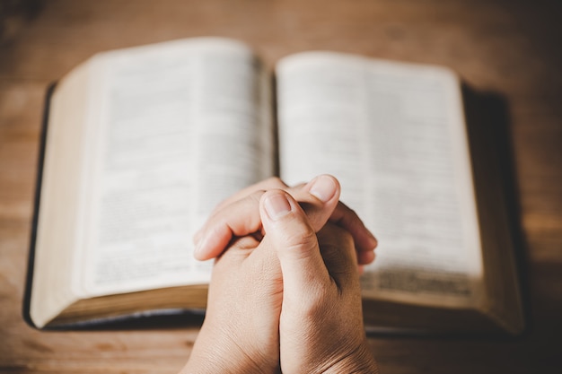 Spiritualiteit en religie, handen gevouwen in gebed op een heilige bijbel in kerkconcept voor geloof.