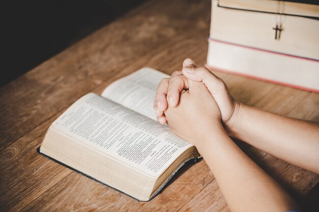 Spiritualiteit en religie, handen gevouwen in gebed op een Heilige Bijbel in kerkconcept voor geloof.