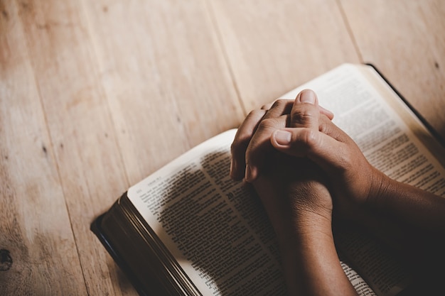 Spiritualiteit en religie, handen gevouwen in gebed over een Heilige Bijbel in kerk-concept voor geloof.