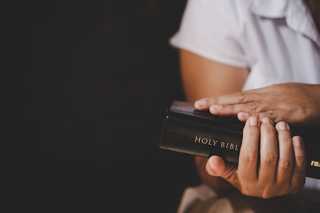 Spiritualiteit en religie, handen gevouwen in gebed over een Heilige Bijbel in kerk-concept voor geloof.