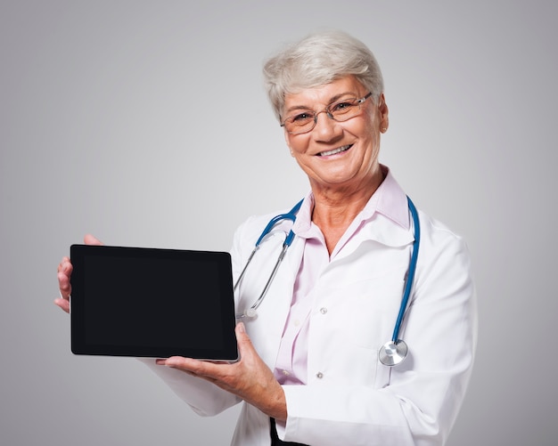 Spontane vrouwelijke arts die scherm van digitale tablet toont