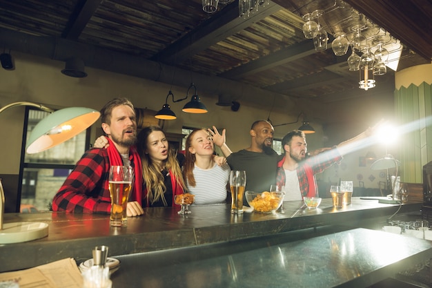 Sportfans juichen in bar, pub en drinken bier terwijl kampioenschap, competitie gaat