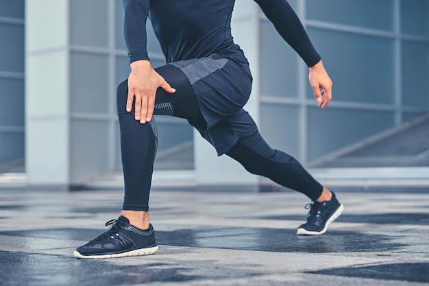 Sportieve atletische man warmt zich op en strekt zich buiten uit over de achtergrond van een modern gebouw.