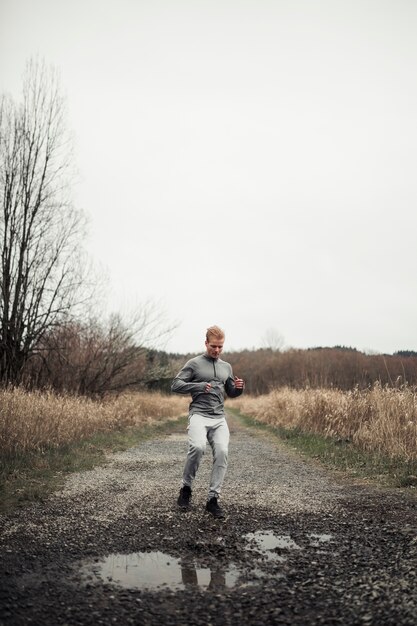 Sportieve jonge mannelijke atleet die op landweg loopt