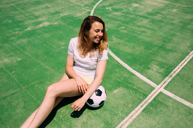 Sportieve jonge vrouw zit met voetbal
