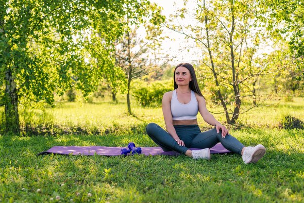 Sportieve jonge vrouw zittend op een sportmat en ontspannen na een training buitenshuis