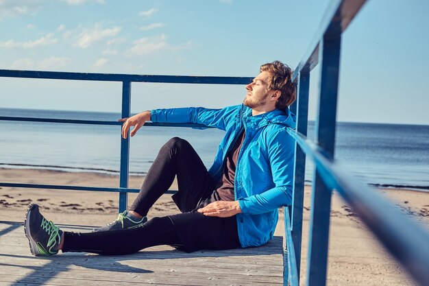 Sportieve jongeman is aan het chillen in de buurt van zee terwijl hij op een zonnige dag op het balkon zit.