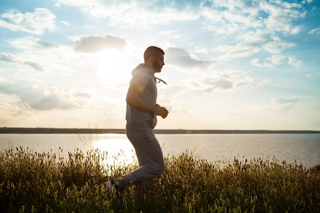 Sportieve jongeman joggen in veld bij zonsopgang.