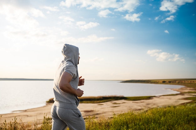 Sportieve jongeman joggen in veld bij zonsopgang.