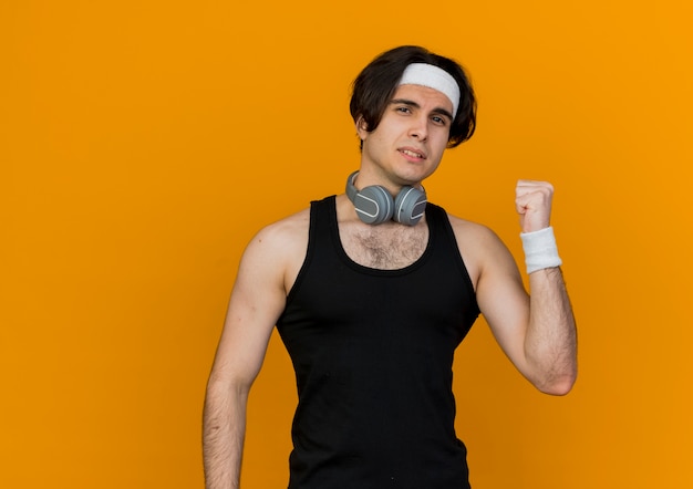 Sportieve jongeman met sportkleding en hoofdband met koptelefoon om nek met zelfverzekerde uitdrukking naar achteren