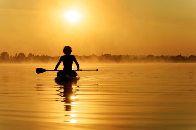 Sportieve jongeman zittend op sup board met lange peddel