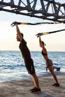 Gratis foto sportieve jongeren trainen met trx in de buurt van de zee in de ochtend.
