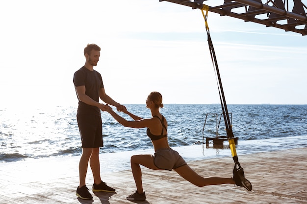 Sportieve jongeren trainen met trx in de buurt van de zee in de ochtend.