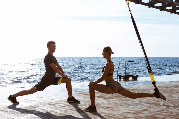 Sportieve jongeren trainen met trx in de buurt van de zee in de ochtend.