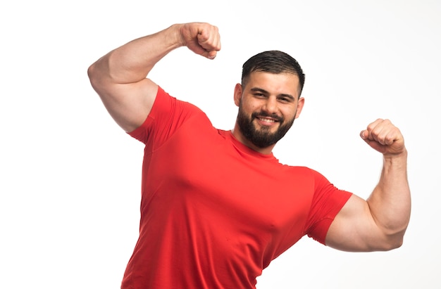 Sportieve man in rood shirt toont zijn armspieren en ziet er zelfverzekerd uit.