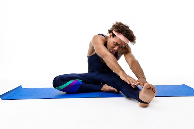 Sportieve man uitrekken, zittend op yoga mat