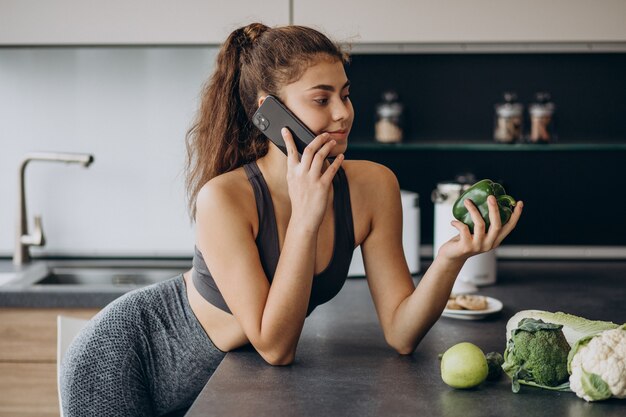 Sportieve vrouw bij keuken met behulp van mobiele telefoon