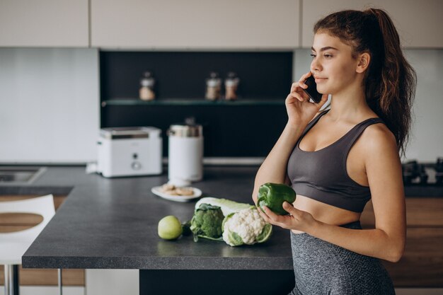 Sportieve vrouw bij keuken met behulp van mobiele telefoon