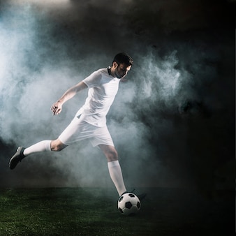 Sportman die voetbalbal in rook schoppen