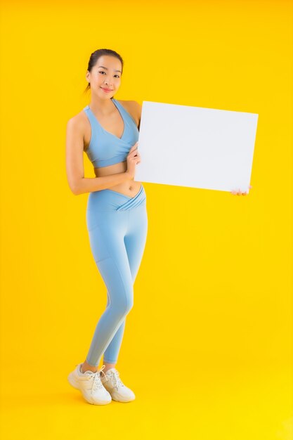 Sportwear toont de portret mooie jonge Aziatische vrouw sportwear leeg wit aanplakbord op geel