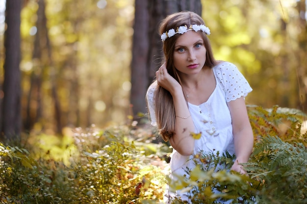 Sproeterige vrouw met een bloemcirkel op haar hoofdportret in de herfstbos in een daglicht.