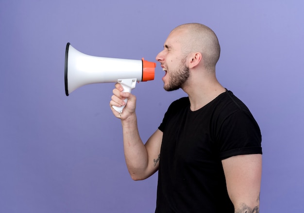 Staande in profiel bekijken sportieve jongeman spreekt op luidspreker geïsoleerd op paars