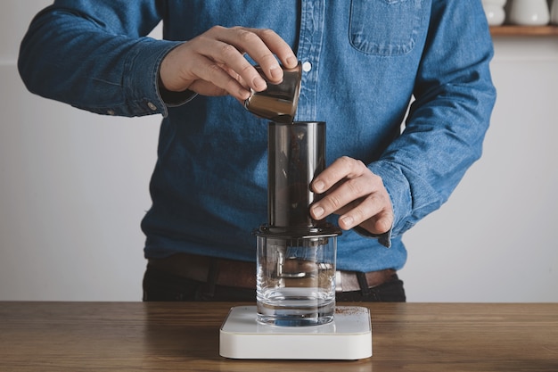 Gratis foto stap voor stap aero pers koffiebereiding barista in spijkerbroek shirt giet gemalen koffiepoeder van stalen beker naar aeropress professionele koffiebrouwerij caféwinkel