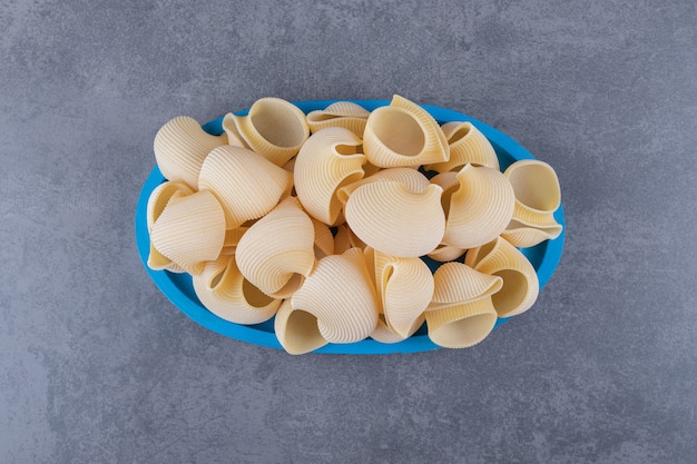 Gratis foto stapel conchiglie pasta op blauw bord.