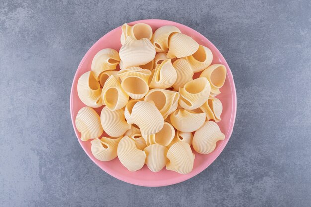 Stapel conchiglie pasta op roze plaat.
