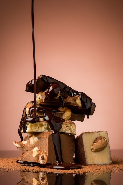 Stapel gebroken chocolade op tafel tegen bruine studioachtergrond en warme chocoladespray