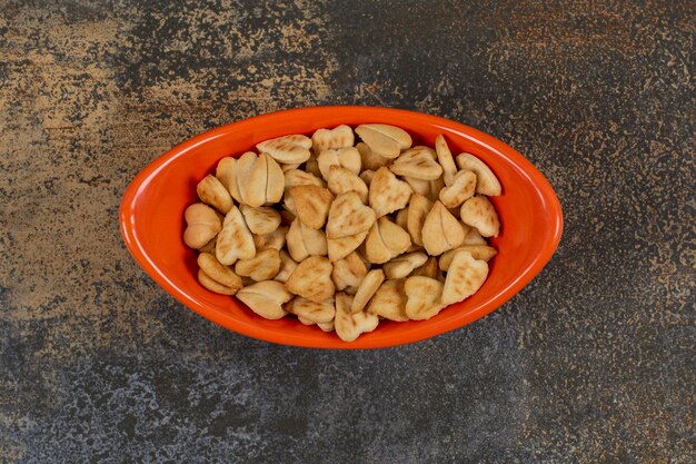 Stapel hartvormige zoute crackers in oranje kom.