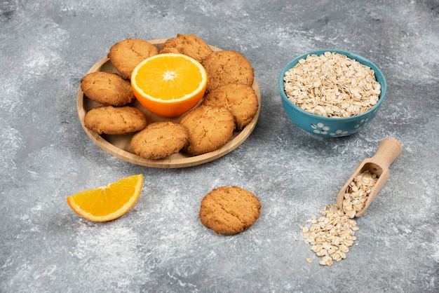 Stapel koekje met sinaasappel op een houten bord en havermout in een kom.