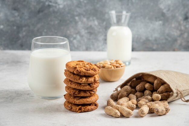 Stapel koekjes met honing, melk en pinda's op marmeren tafel.