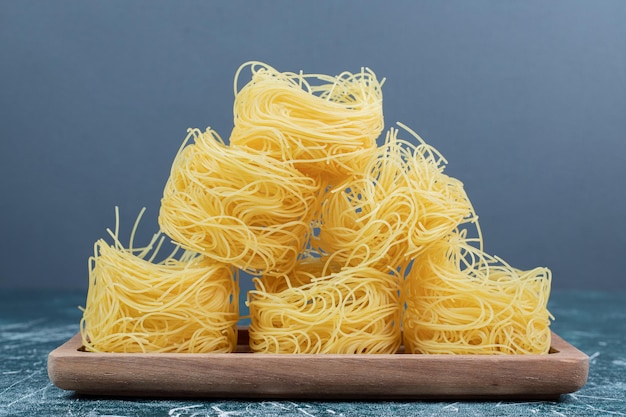 Stapel rauwe spaghetti nesten op een houten bord.