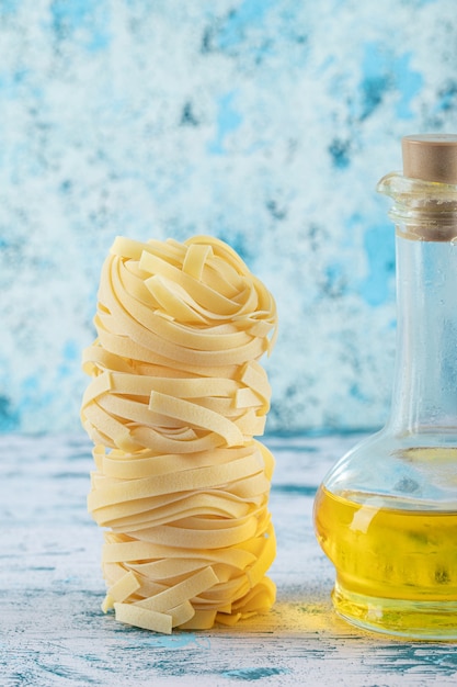 Gratis foto stapel tagliatelle-nesten en glas olijfolie op blauwe achtergrond. hoge kwaliteit foto