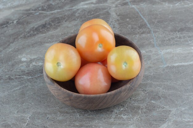 Stapel verse tomaten in houten kom over grijze tafel.