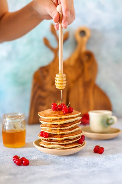 Stapel zelfgemaakte pannenkoeken met honing siroop en bessen.