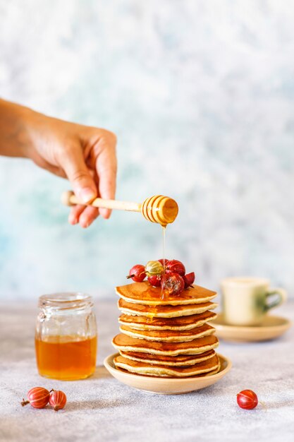 Stapel zelfgemaakte pannenkoeken met honing siroop en bessen.