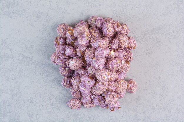 Stapel zoete popcorn bedekt met paars snoep op marmer.