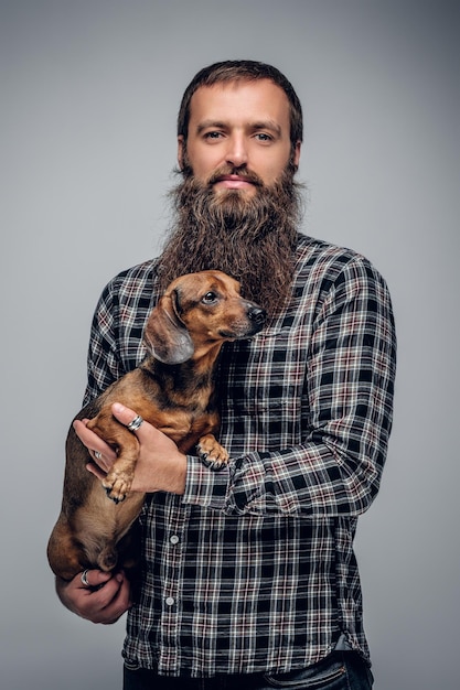 Stedelijke bebaarde man gekleed in een geruit hemd houdt een schattige dassenhond vast.