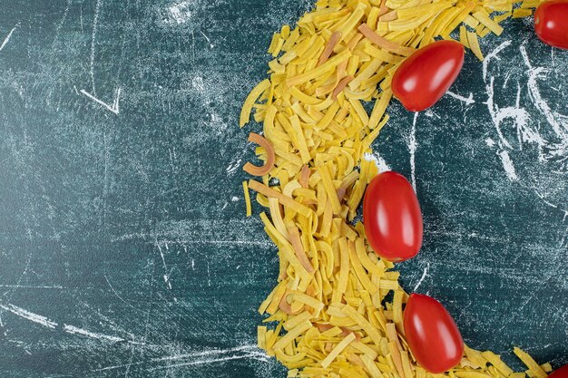 Stelletje rauwe pasta op blauwe ruimte met tomaten.