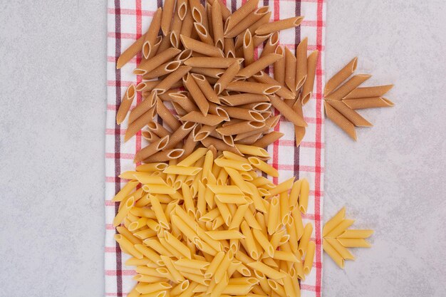 Stelletje rauwe penne pasta op gestreept tafelkleed.