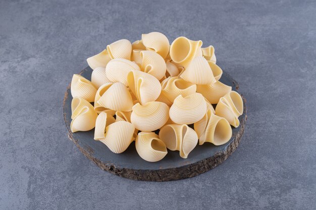 Stelletje rauwe shell pasta op stuk hout.