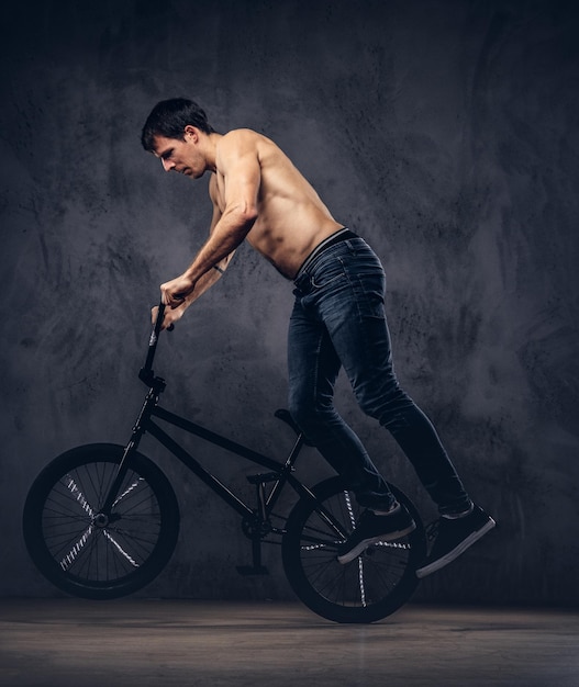 Gratis foto sterke shirtloze man, maakt een acrobatisch figuur met bmx in een studio. geïsoleerd op een donkere achtergrond.